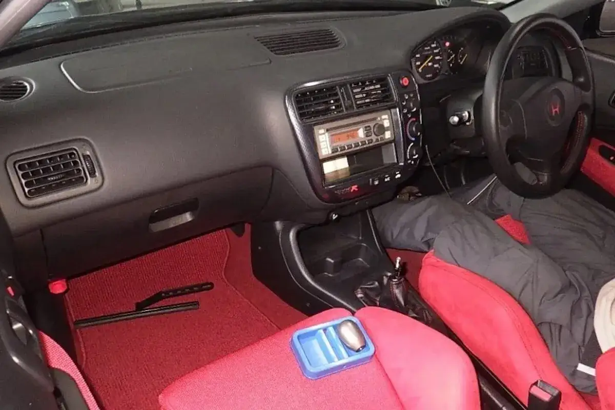 Wnętrze kultowego Honda Civic EK9 z czerwonymi fotelami i dywanikami. Widoczna deska rozdzielcza, radio i kierownica.
