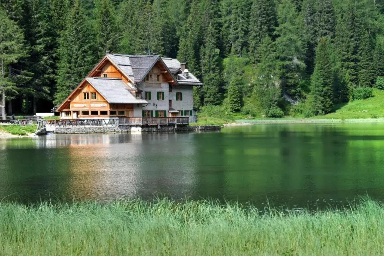 Rifugio sul **lago Nambino**, circondato da fitti boschi di conifere e verdi pascoli.