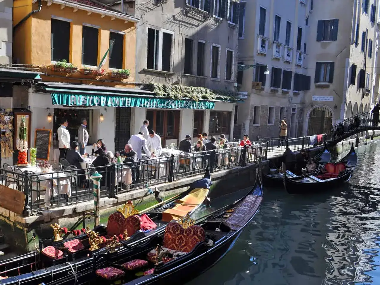 Gondole ormeggiate vicino a ristoranti famosi a Venezia, con persone sedute ai tavoli all'aperto.