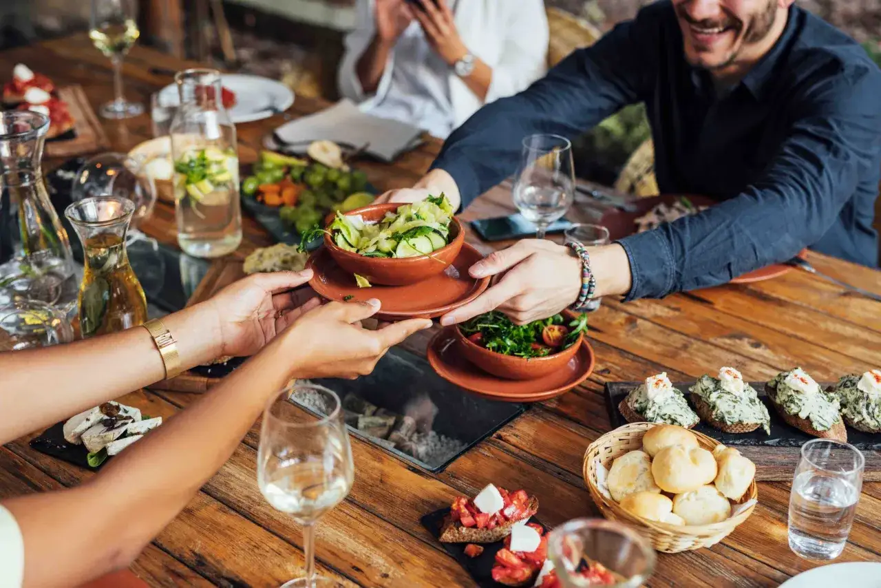 Ein fröhlicher **restaurant besuch** mit Freunden. Sie teilen sich Salate und Bruschetta an einem Holztisch, dazu gibt es Wein und Wasser.