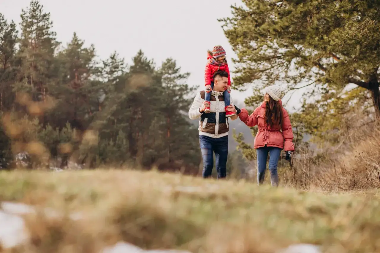 Radosne wakacje dla dzieci: ojciec niesie córkę na barana, mama trzyma go za rękę, spacerują po lesie.