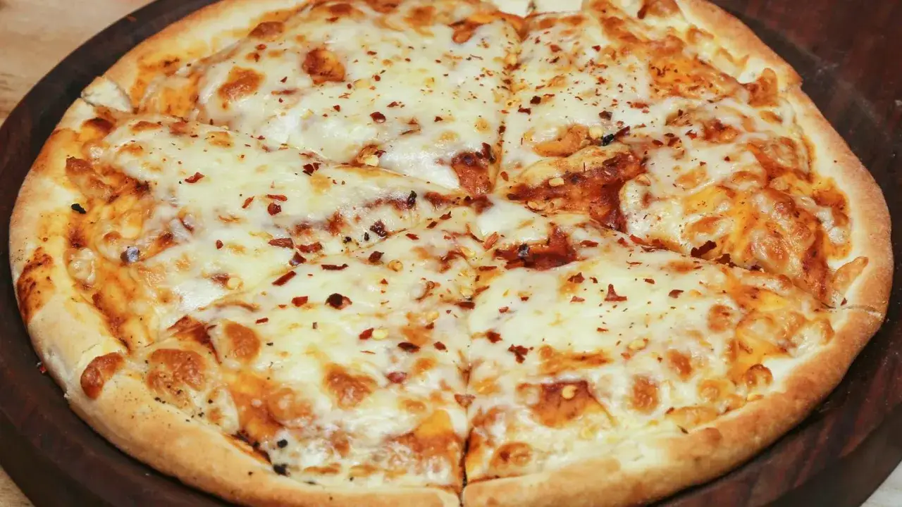 Pyszna pizza bez drożdży, obficie posypana serem i płatkami chili, pokrojona na kawałki.