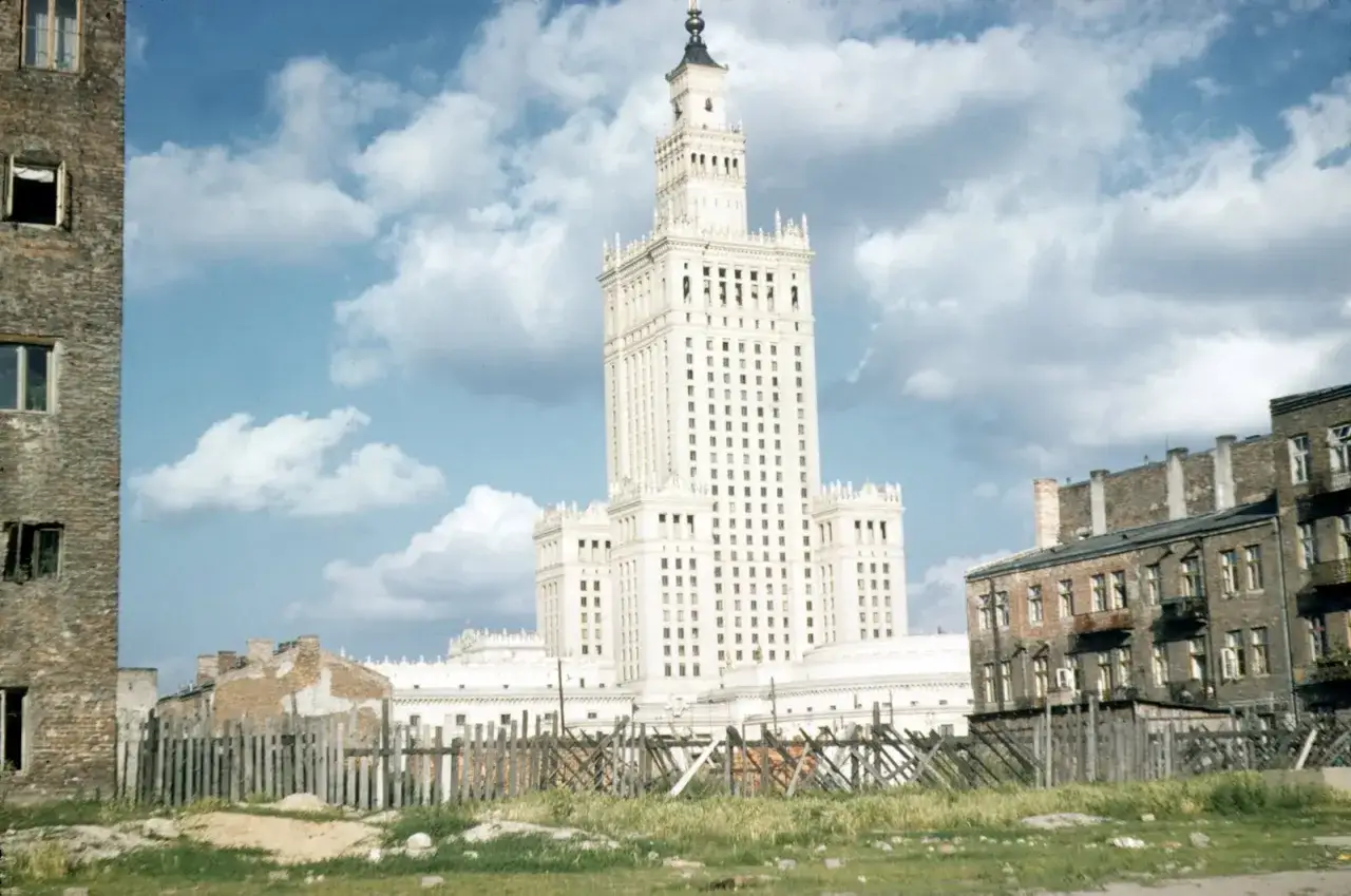 Budowa Pałacu Kultury i Nauki w Warszawie. W tle monumentalny budynek, na pierwszym planie zniszczone kamienice i prowizoryczne ogrodzenie.