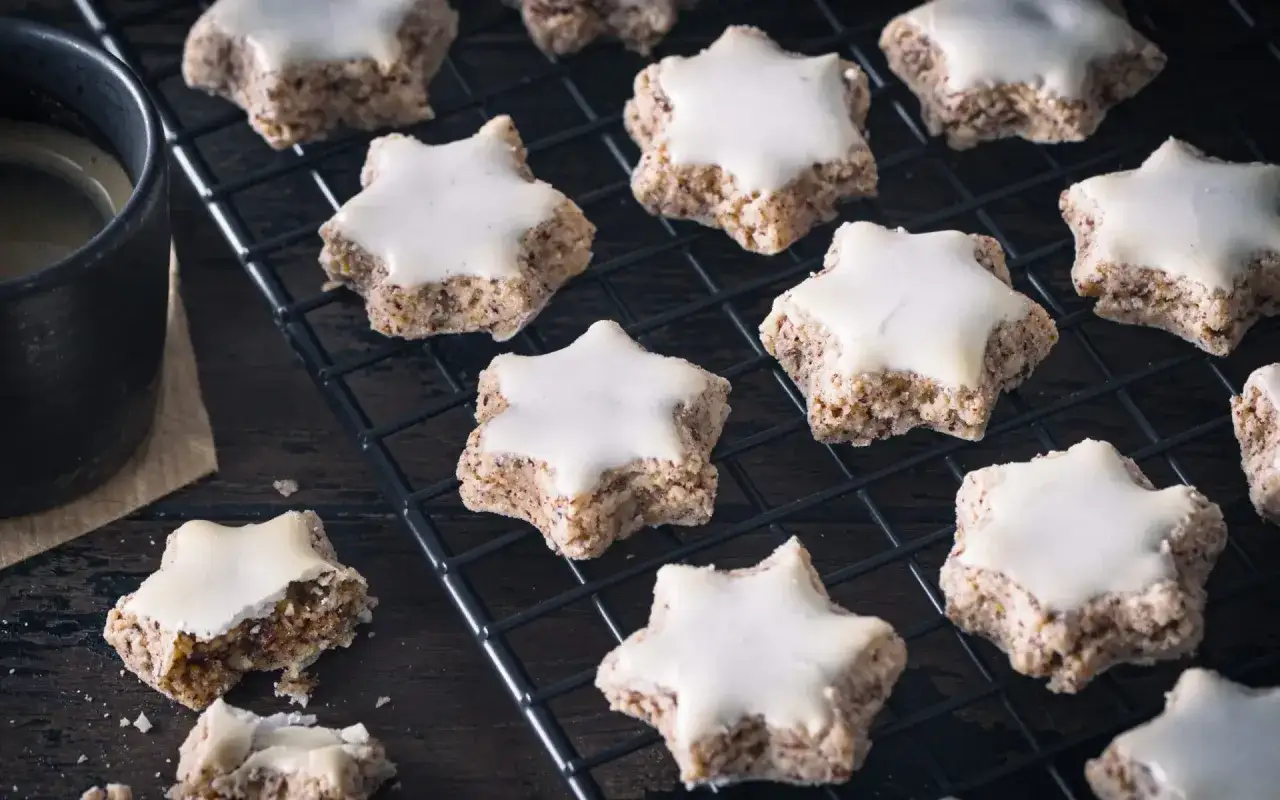 Zimtsterne rezept einfach schnell: Sterne-Pl&auml;tzchen mit wei&szlig;er Glasur auf einem Gitter, daneben eine Tasse Kaffee.