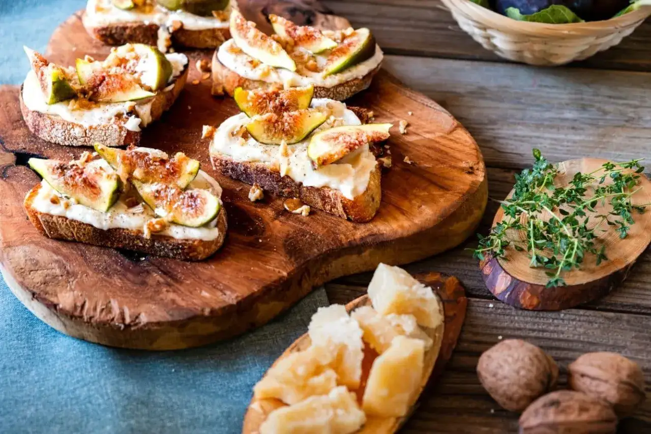 Bruschette con fichi freschi e una cremosa fonduta di parmigiano, guarnite con noci e timo.