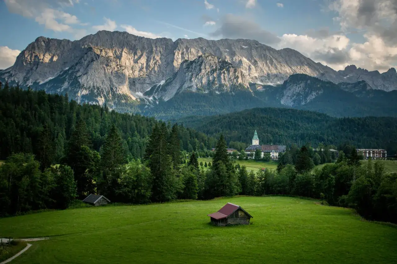 Majestätische Berge überblicken das Schlosshotel Wernersdorf, eingebettet in grüne Wälder und Wiesen mit einer kleinen Hütte.
