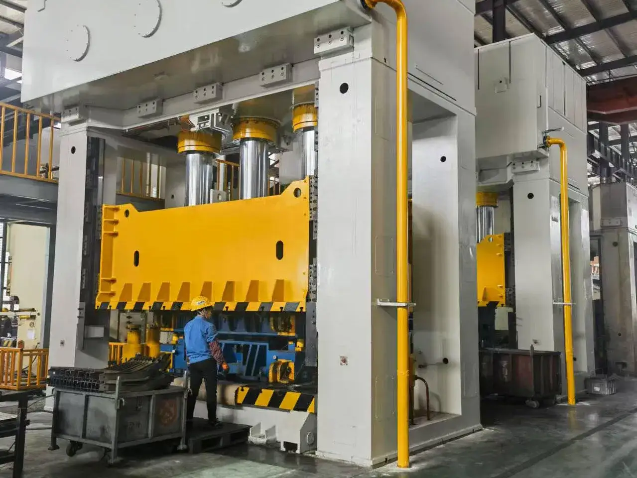 Pracownik w kasku przy wielkiej prasie hydraulicznej, kluczowej dla producenta części samochodowych.