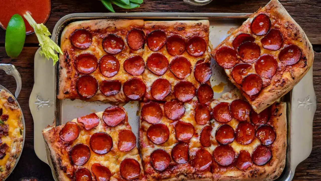 Saftige Pizza vom Blech mit vielen runden Pepperoni-Scheiben, goldbraun gebacken und bereit zum Genie&szlig;en.