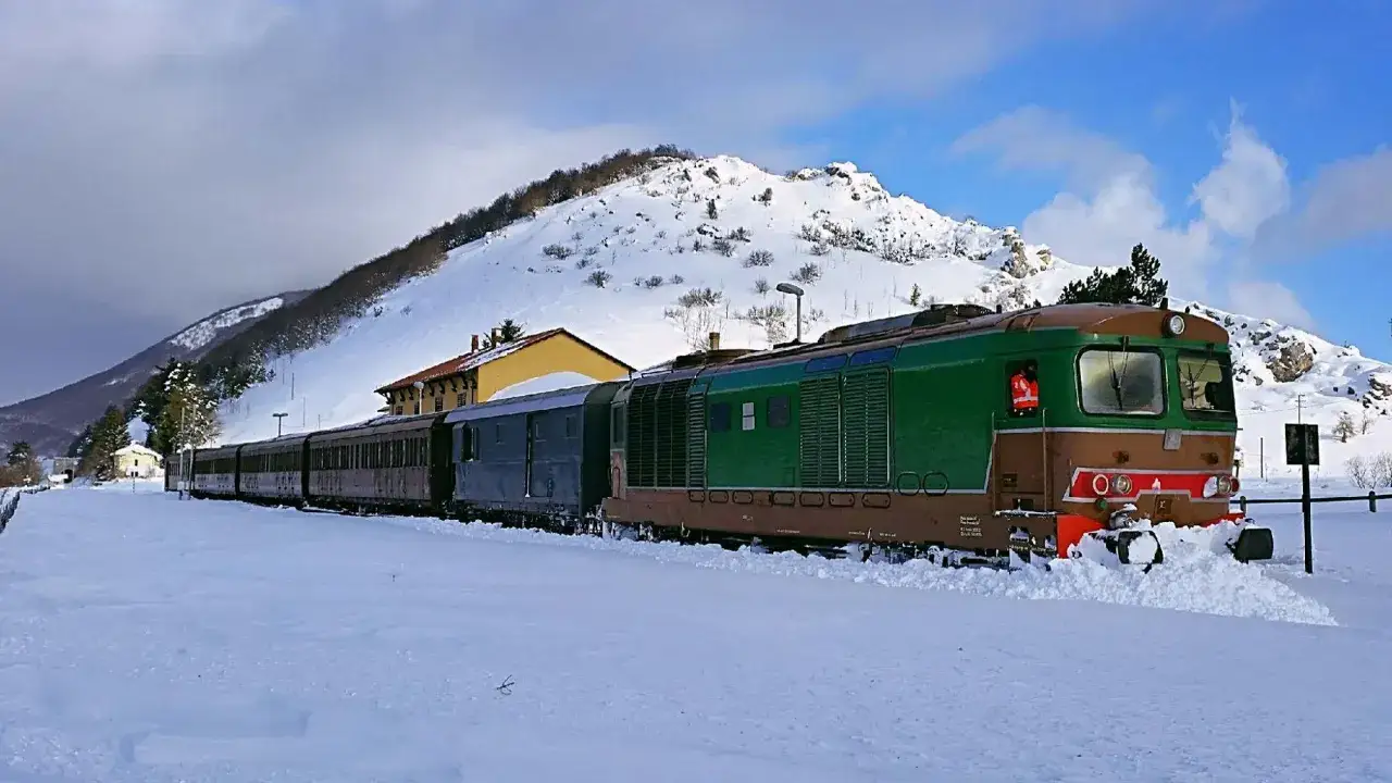 Treno fermo nella neve, con montagne innevate sullo sfondo. Un assaggio delle tappe della Transiberiana d'Abruzzo in inverno.