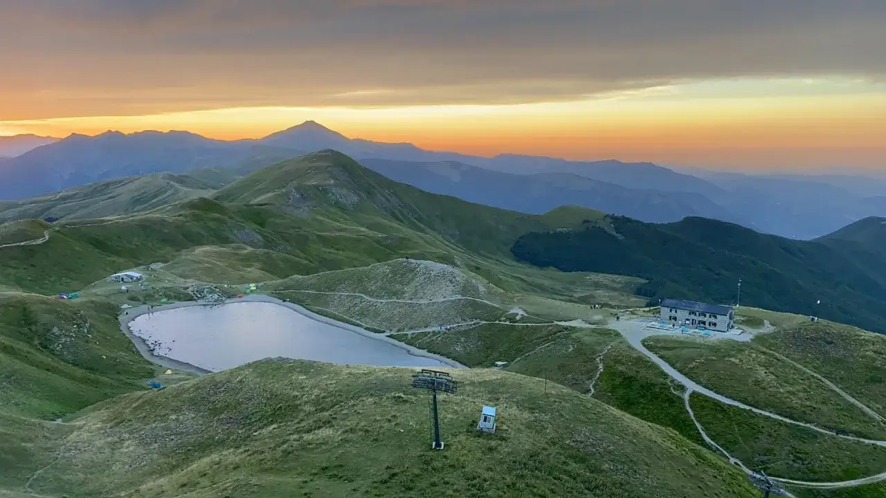 Alba sulle montagne con lago e rifugi in Emilia Romagna. Tende sparse e un edificio in pietra, con un impianto di risalita.
