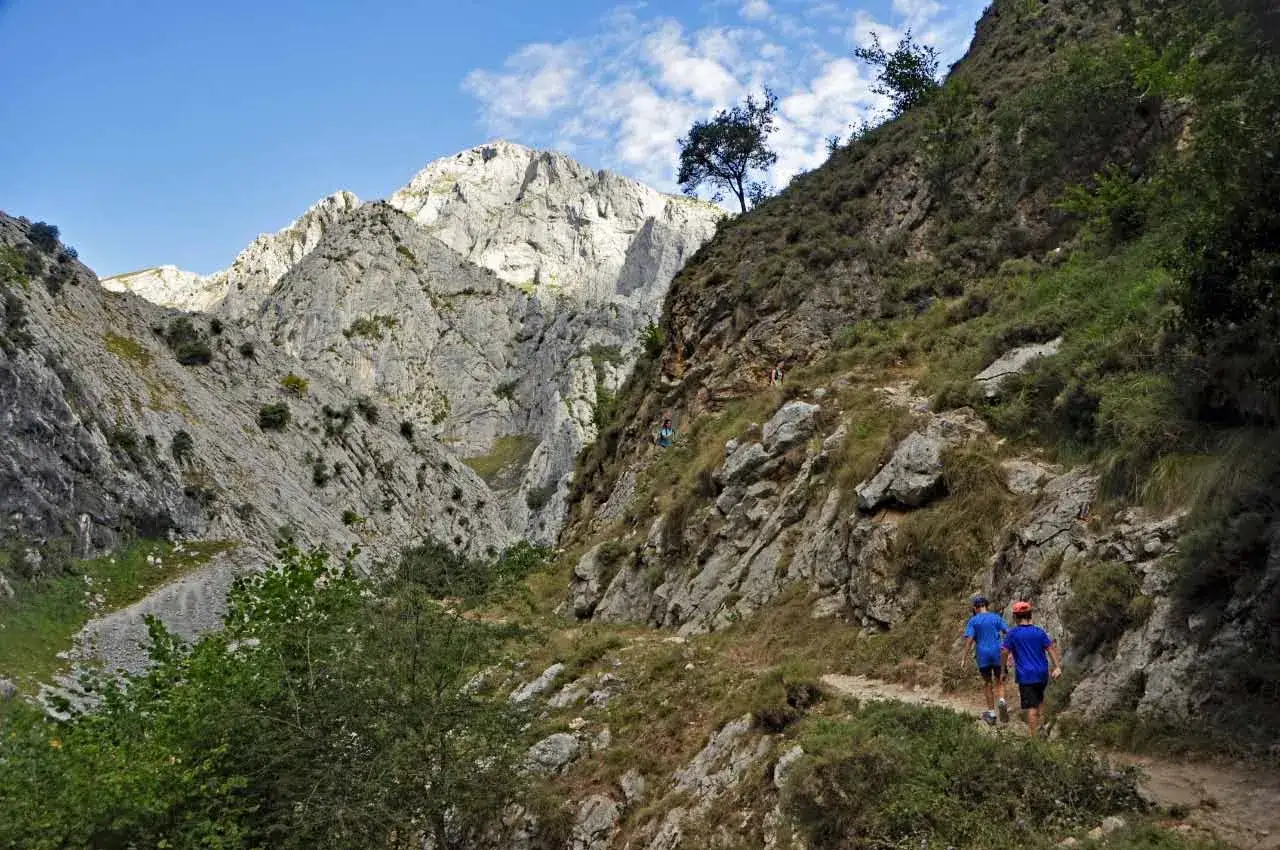 Dos niños disfrutan de la ruta Poncebos - Bulnes con niños, caminando por un sendero rocoso entre imponentes montañas.