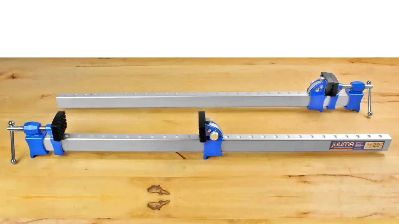 Deux serre-joints de menuiserie, bleus et argent&eacute;s, pr&ecirc;ts pour un collage du bois sur une surface en bois clair.