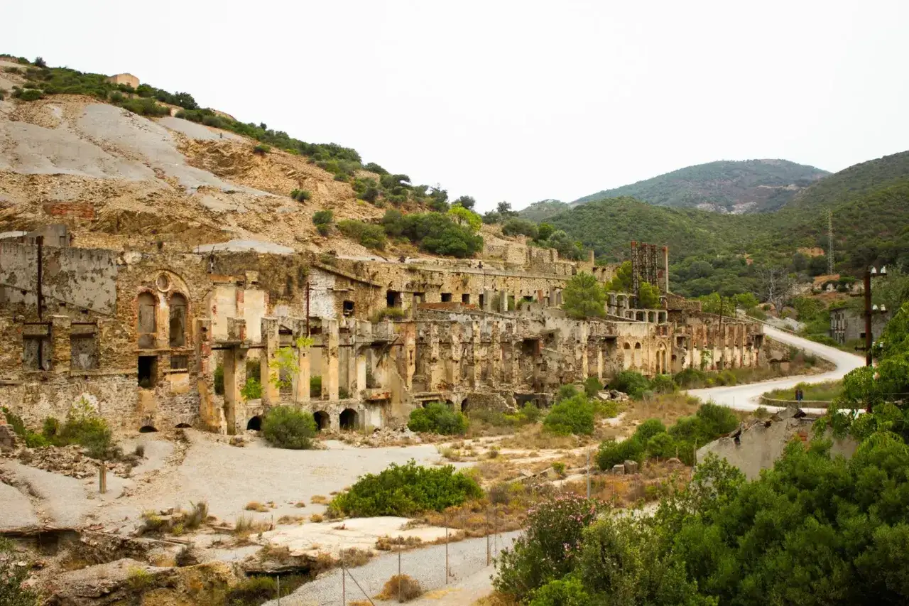 Rovine di un'antica zona mineraria sarda, con edifici diroccati e vegetazione che si riappropria del paesaggio.