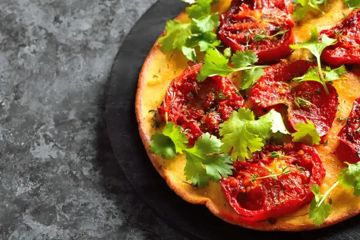 Une socca dorée garnie de tomates rôties et de coriandre fraîche. Une recette simple et savoureuse pour un apéritif méditerranéen.