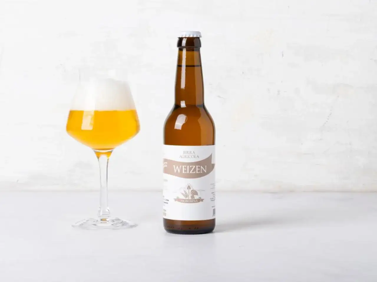 Bicchiere di birra hefeweizen con schiuma abbondante accanto a una bottiglia della stessa birra.