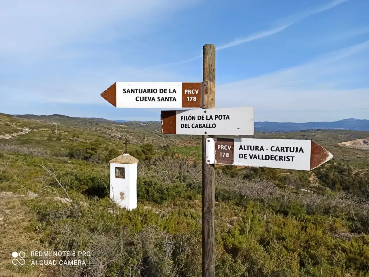 Señalización de senderos en un paisaje montañoso. Indica rutas a Santuario de la Cueva Santa, Pilón de la Pota del Caballo y Altura - Cartuja de Valldecrist. Ideal para quienes disfrutan de **que ver en altura**.