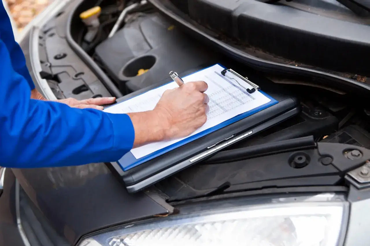Tecnico con cartella in mano, controlla i dati per la verifica veicoli rubati sotto il cofano aperto di un'auto.