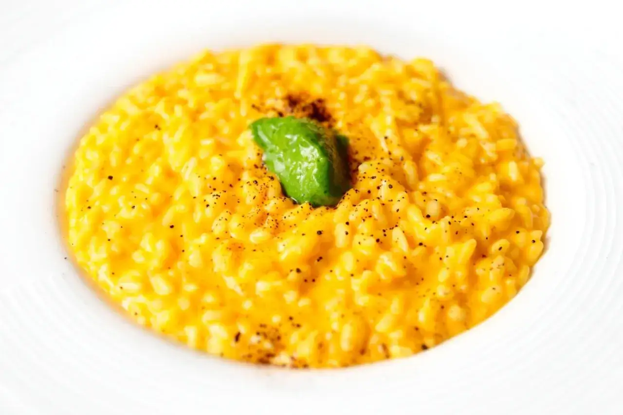 Un cremoso risotto alla milanese, dal colore giallo intenso, guarnito con una fogliolina verde e pepe nero macinato.