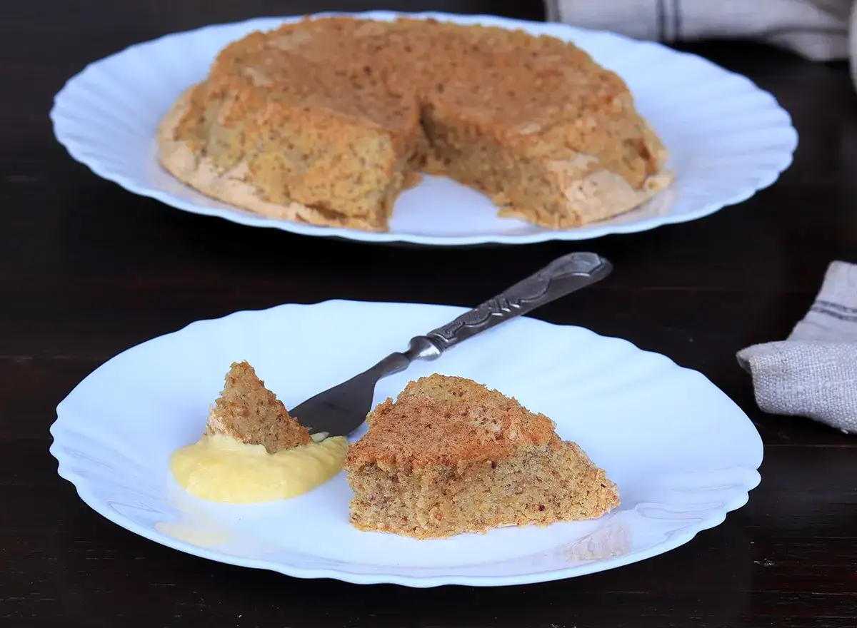 Una fetta di torta nocciole piemontese originale, con crema gialla e un pezzetto su una forchetta.