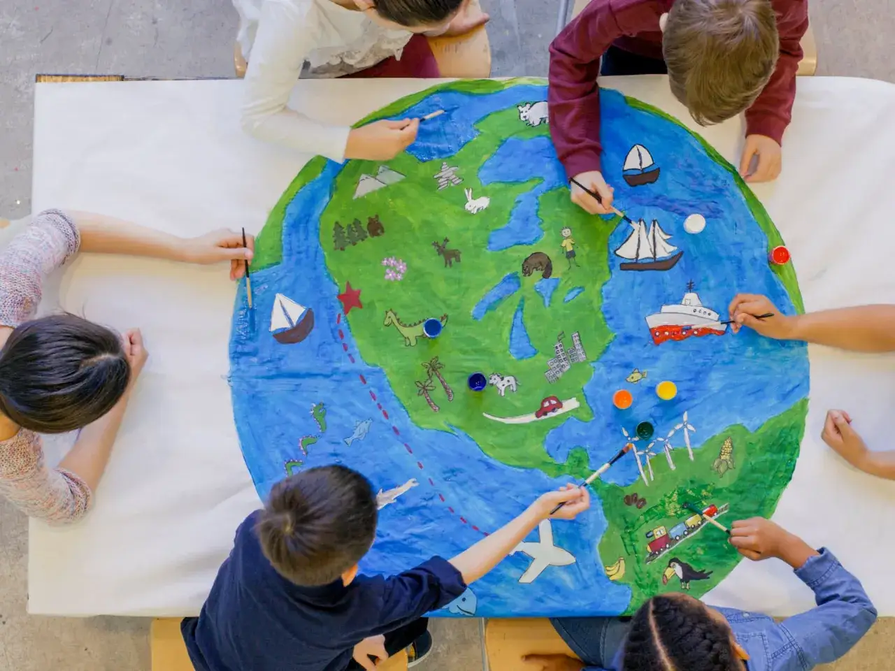 Niños pintan un mapa del mundo, creando **imágenes para describir** la vida en la Tierra: animales, barcos, autos y molinos de viento.