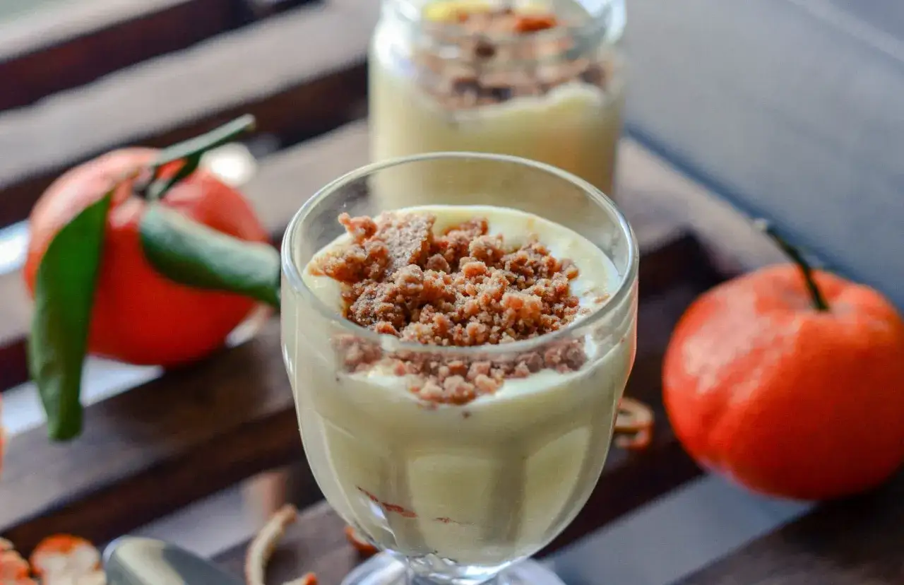 Délicieuse mousse clémentine mascarpone, garnie de miettes croustillantes, avec des clémentines fraîches en arrière-plan.
