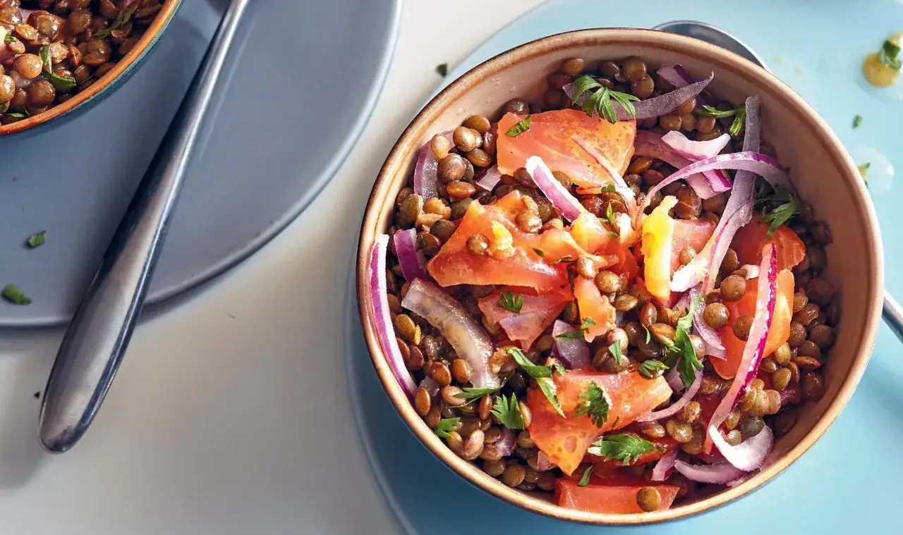 Salade de lentilles savoureuse avec des morceaux de saumon, des oignons rouges et du persil frais. Un plat color&eacute; et nutritif.