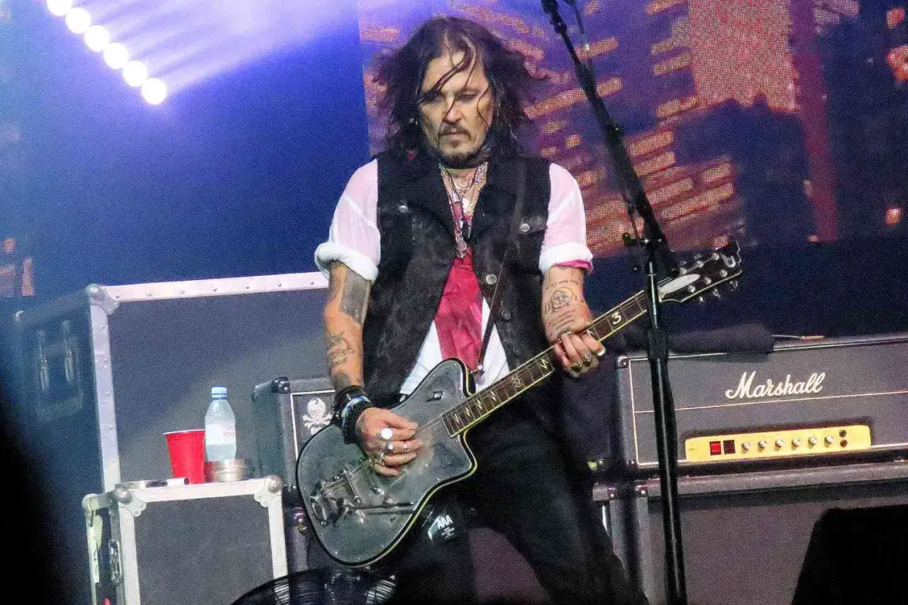 Johnny Depp gra na gitarze podczas koncertu, jego zespół tworzy rockową atmosferę.