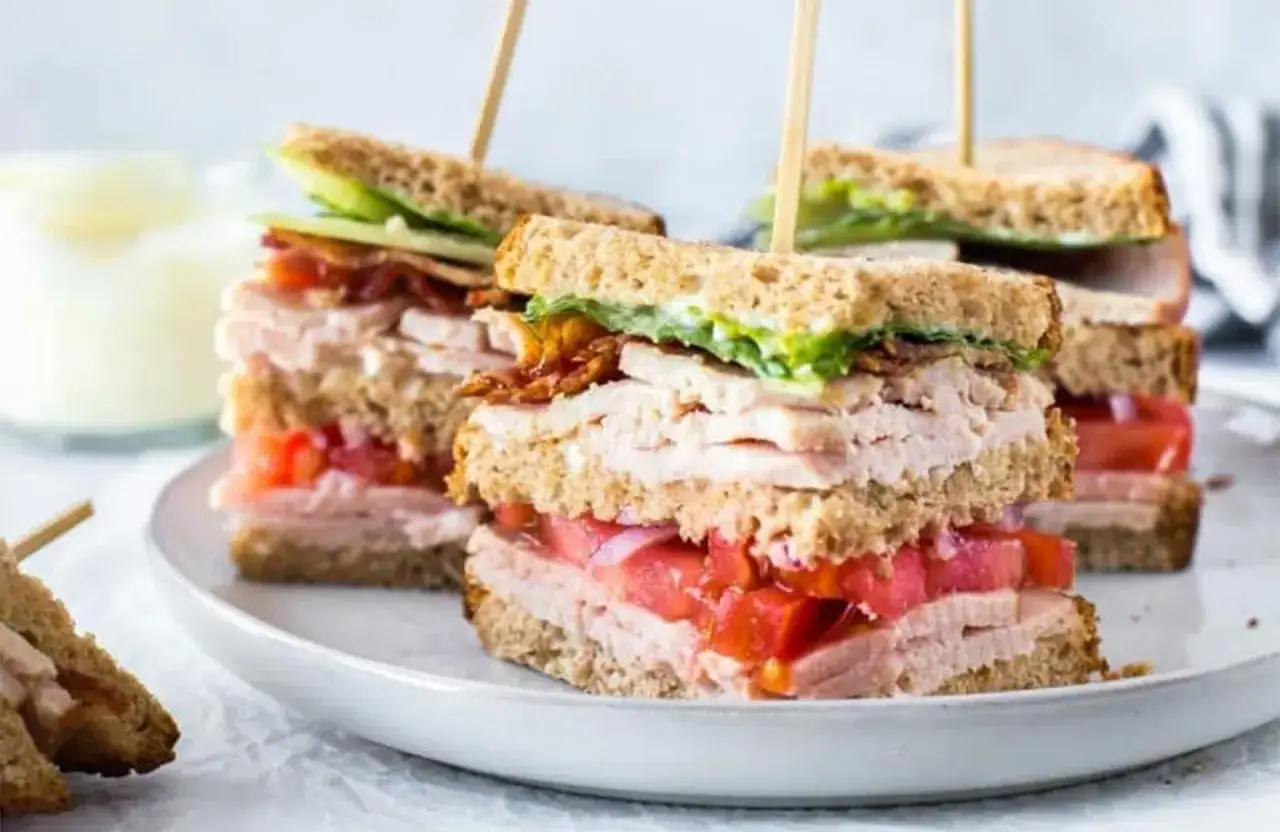 Une excellente idée de sandwich : club sandwich à trois étages avec dinde, bacon, tomates et laitue, piqué avec des brochettes en bois.
