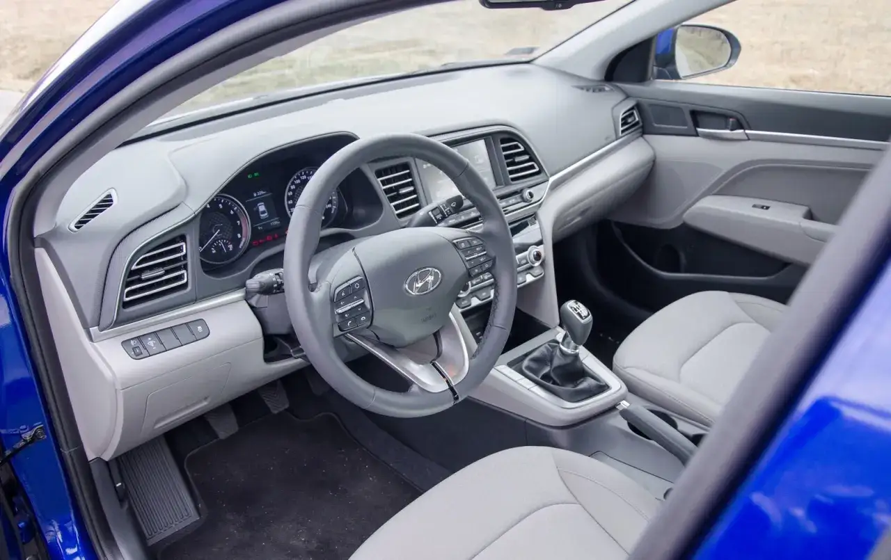 Wnętrze niebieskiego Hyundai sedan: kierownica, deska rozdzielcza z ekranem, dźwignia zmiany biegów i jasne siedzenia.