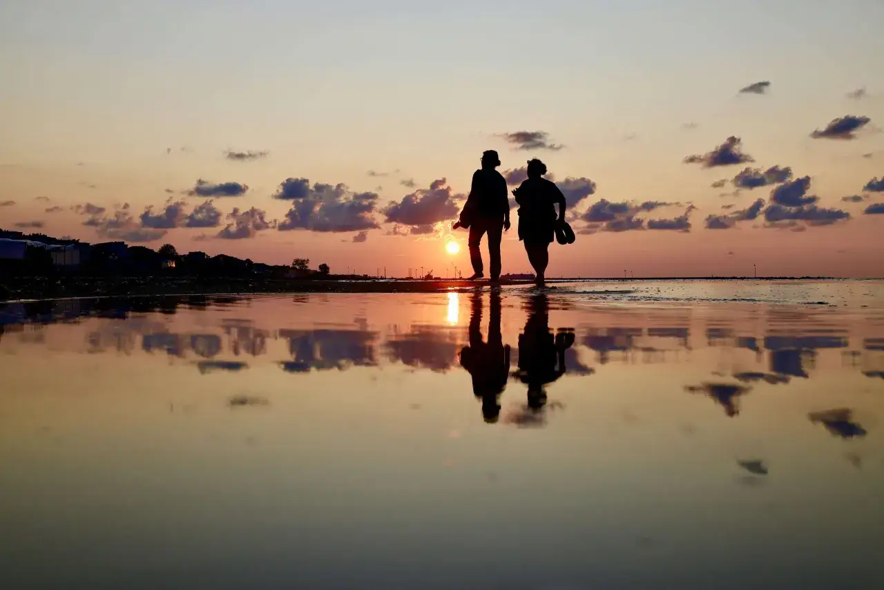 Twee silhouetten lopen langs het strand bij zonsondergang. Een **high sensation seeker en relaties** vinden elkaar in de rust van de natuur.