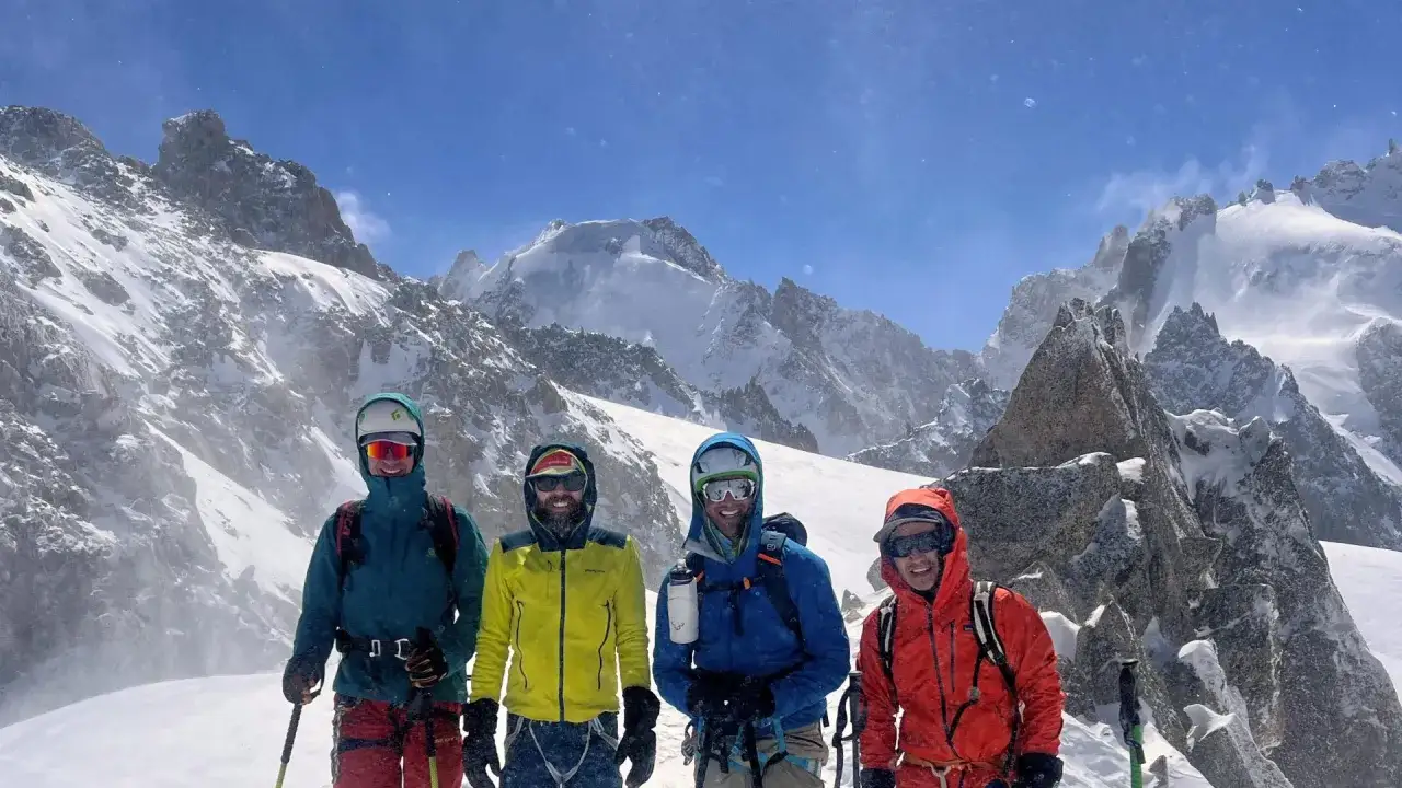 Czterech narciarzy w kolorowych kurtkach na tle ośnieżonych szczyt&oacute;w Alp. Przygotowują się do trudnej trasy Haute Route.