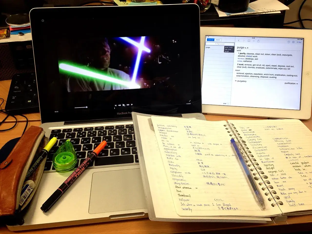 Imparare l'inglese con i film: un MacBook mostra una scena di Star Wars, un iPad con il dizionario e un quaderno pieno di appunti.