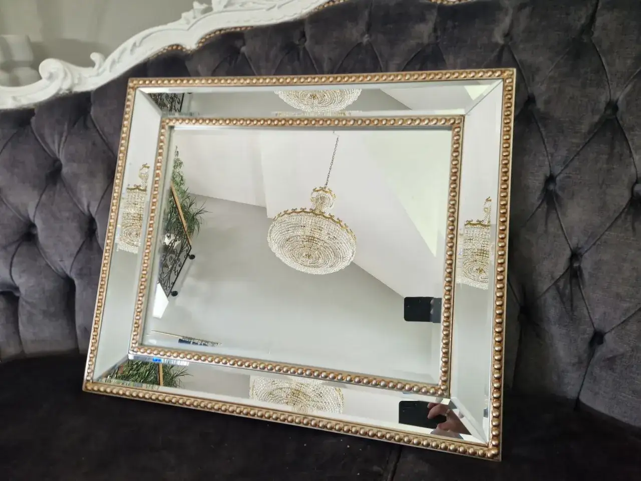 Eleganckie lustro do sypialni glamour z bogato zdobioną złotą ramą, odbijające kryształowy żyrandol.