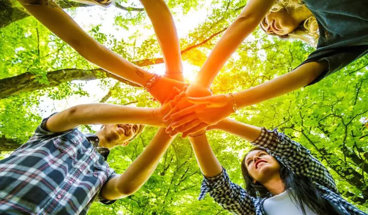 Des mains s'unissent sous un soleil éclatant, symbolisant un jeu ludique adulte et la joie partagée en pleine nature.