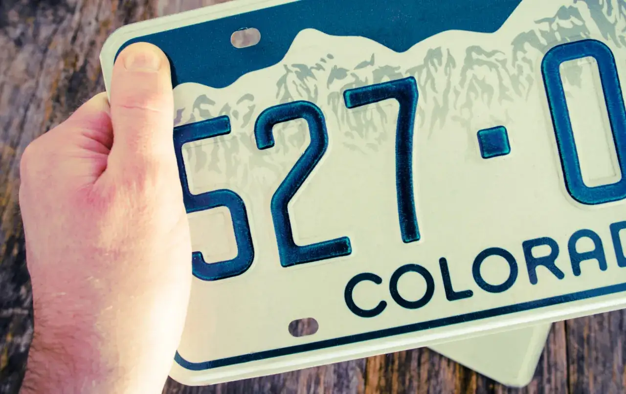 Mano che tiene una targa smarrita del Colorado, numeri 527-0. Posso circolare?
