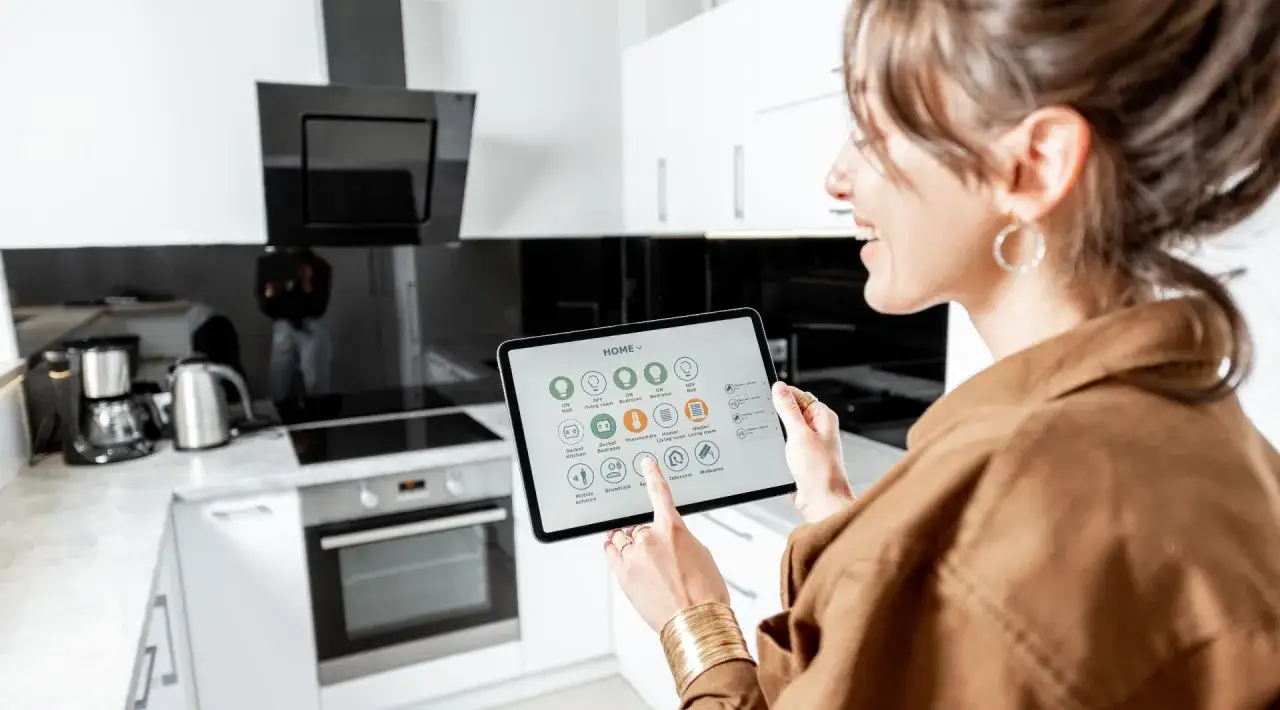Mujer controla electrodomésticos domóticos desde una tablet en una cocina moderna.
