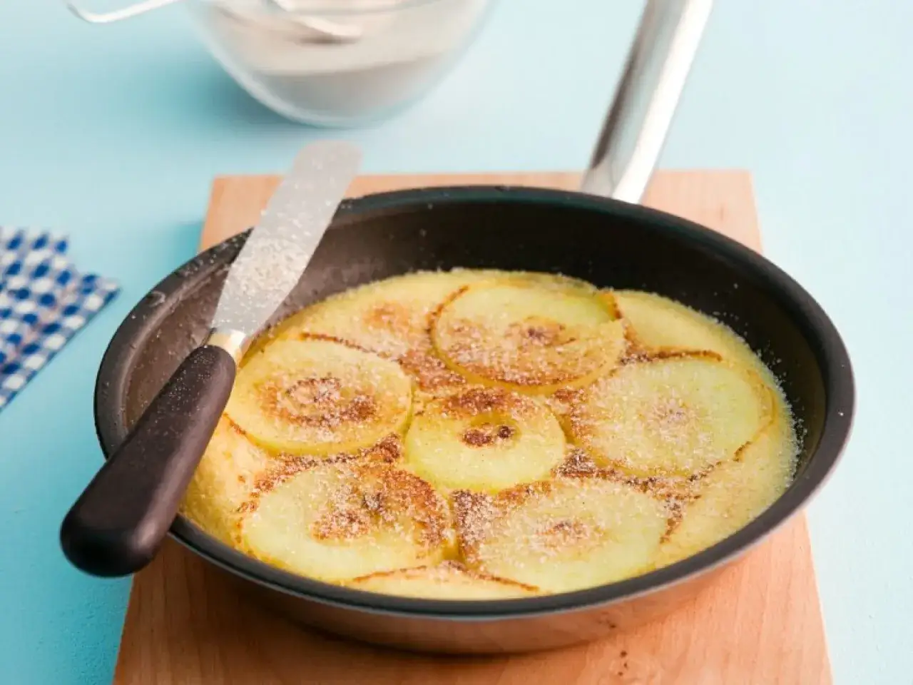 Ein goldbrauner Apfelpfannkuchen im Pfännchen, bestreut mit Zucker. Ein köstliches Apfelpfannkuchen Rezept für Genießer.