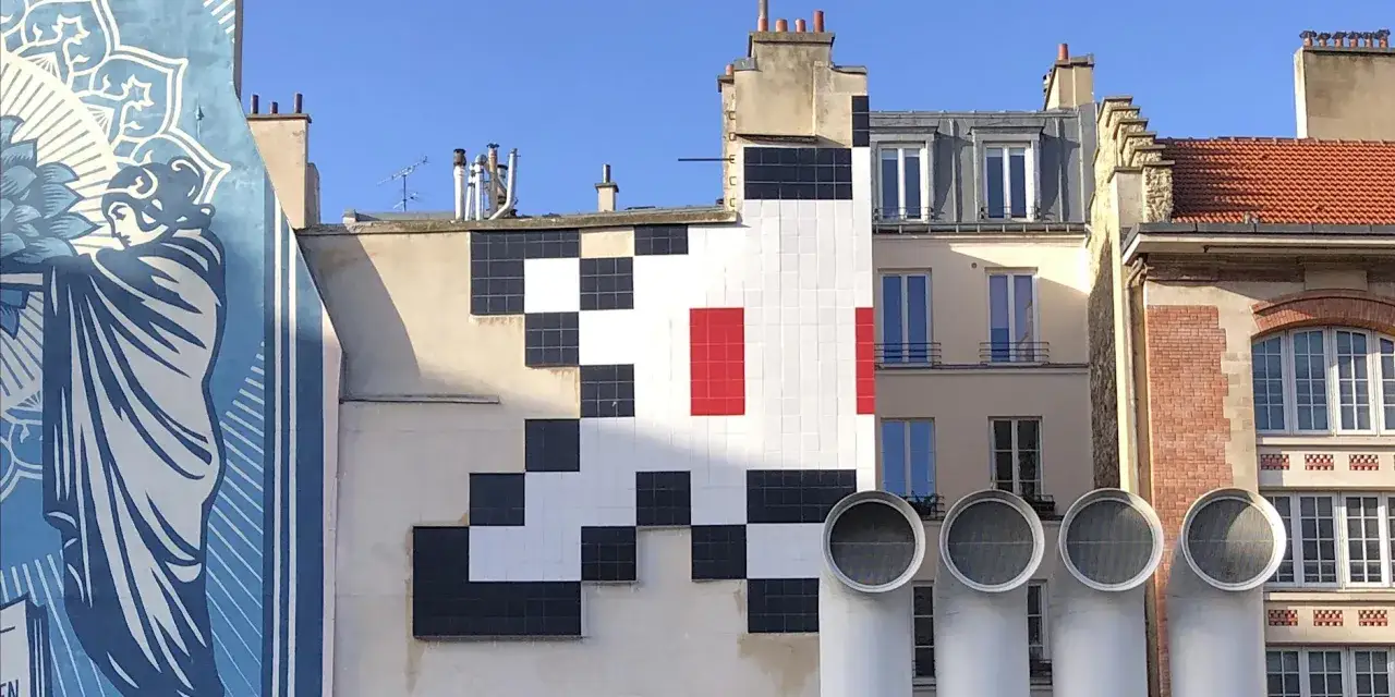 Un Space Invader pixelis&eacute; envahit un mur parisien, &agrave; c&ocirc;t&eacute; d'une fresque bleue.