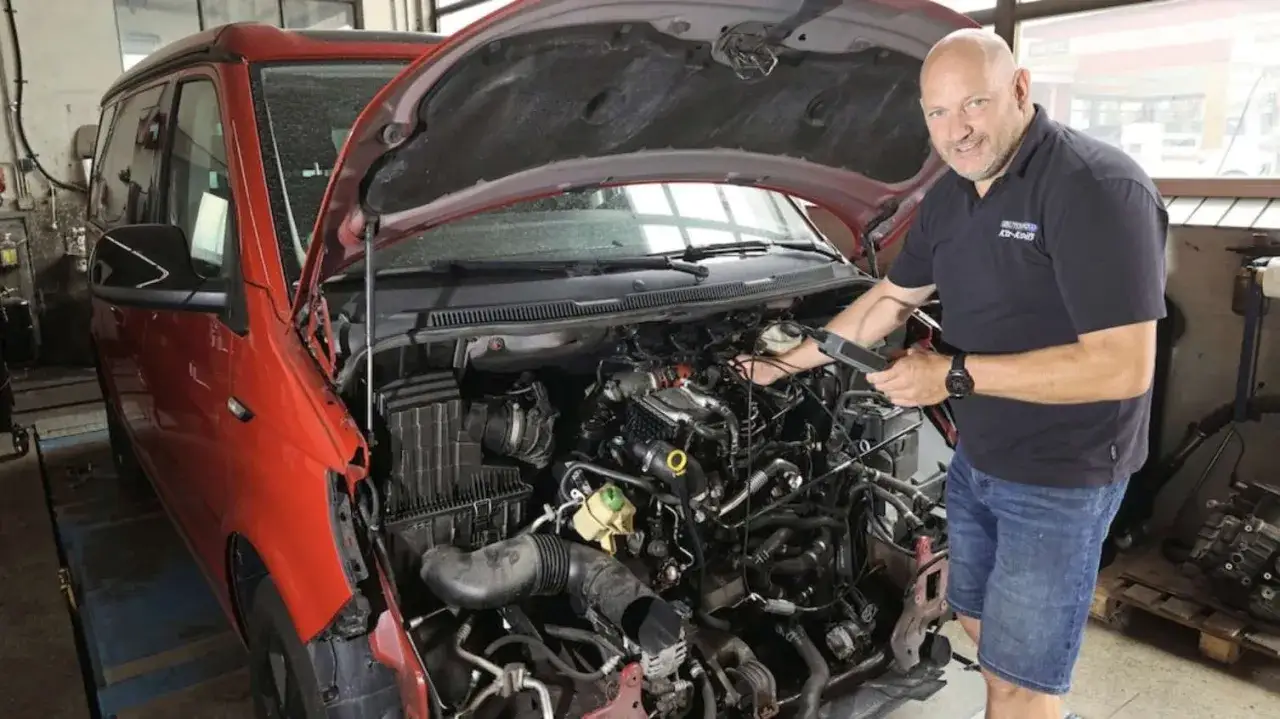 Mechaniker prüft den Motor eines roten VW T6 mit 150 PS auf Probleme.
