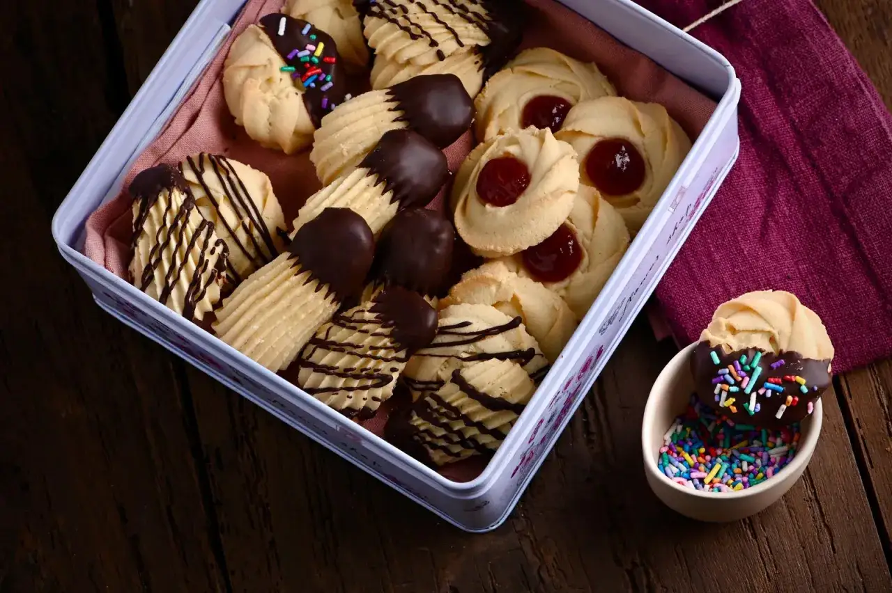 Deliciosas pastas de té en una lata: algunas bañadas en chocolate y con chispas, otras con mermelada y algunas con glaseado de chocolate.