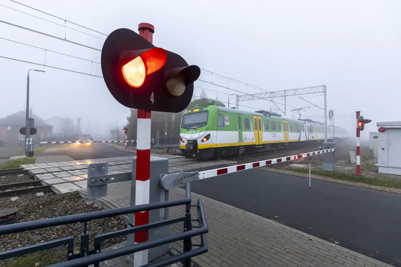 Pociąg zbliża się do przejazdu kolejowego. Czerwone światło sygnalizatora i opuszczone rogatki oznaczają, że transport kolejowy jest w ruchu.
