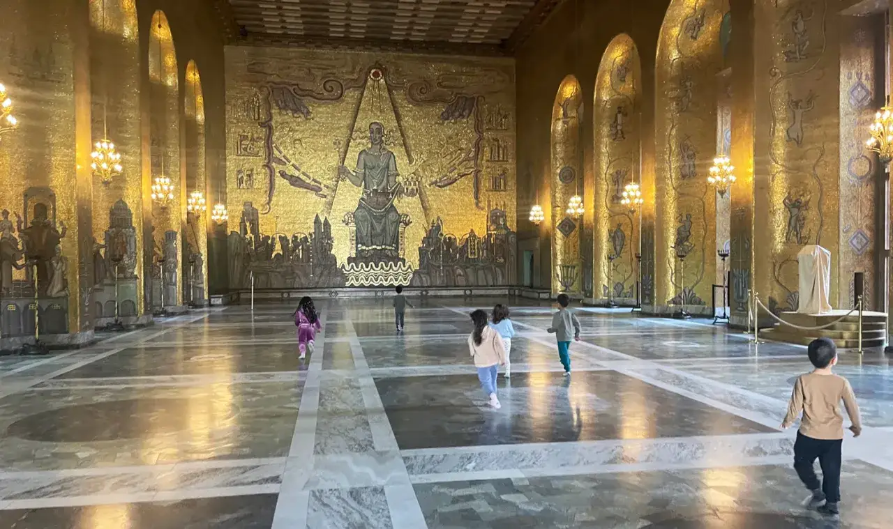 Barn springer genom den gyllene Blå hallen i Stockholms stadshus, beundrar den storslagna mosaiken.