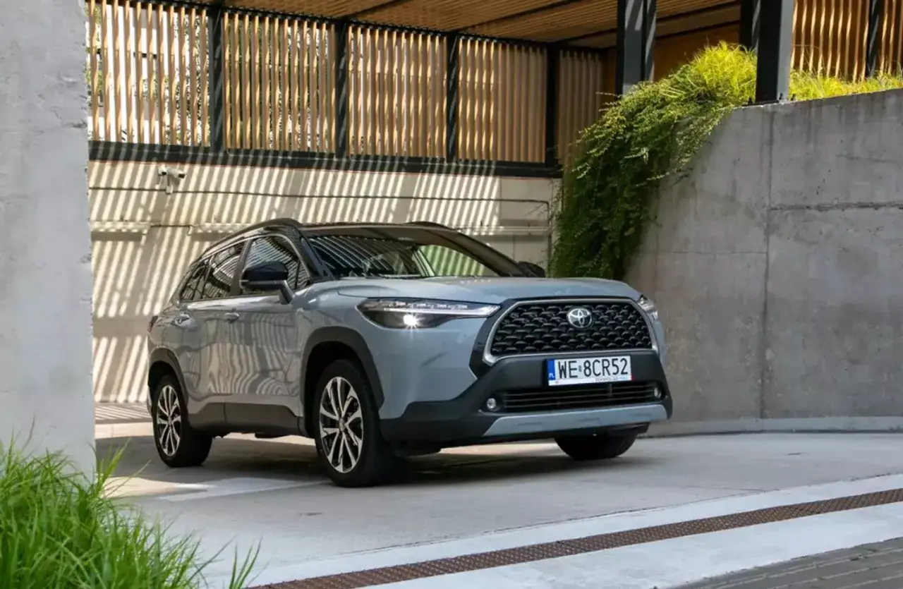Szary SUV Toyota Corolla Cross zaparkowany przed nowoczesnym budynkiem. Idealny wybór na wynajem długoterminowy z wykupem.