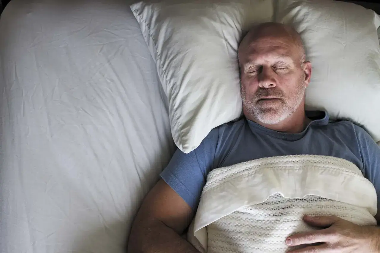 Man sover djupt i en säng, kanske efter en session av progressiv muskelavslappning.