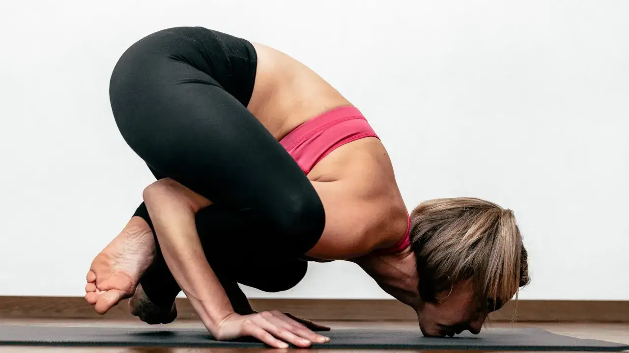 Kobieta w pozycji Bakasana podczas praktyki jogi ashtanga. Skupienie i siła w każdym ruchu.