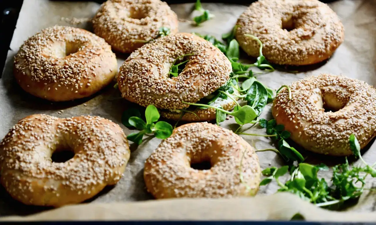 Frisch gebackene Bagels mit Sesam, bereit für ein leckeres Bagel Rezept. Grünzeug liegt dazwischen.