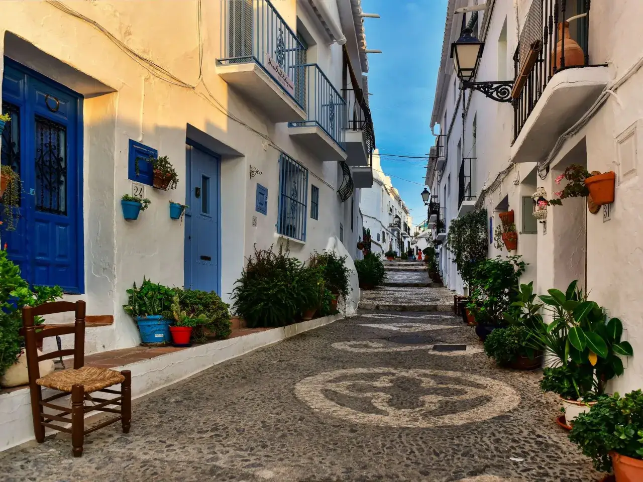 Eine malerische Gasse in Frigiliana, Spanien, mit wei&szlig; get&uuml;nchten H&auml;usern, blauen T&uuml;ren und vielen Pflanzen.