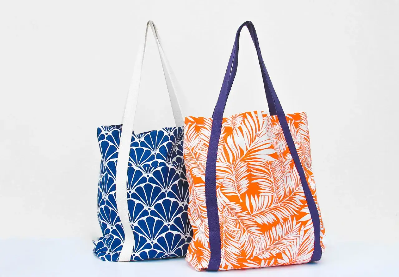 Deux sacs fourre-tout colorés, parfaits pour une idée couture débutant. L'un est bleu avec un motif de coquillages, l'autre orange avec des feuilles de palmier.
