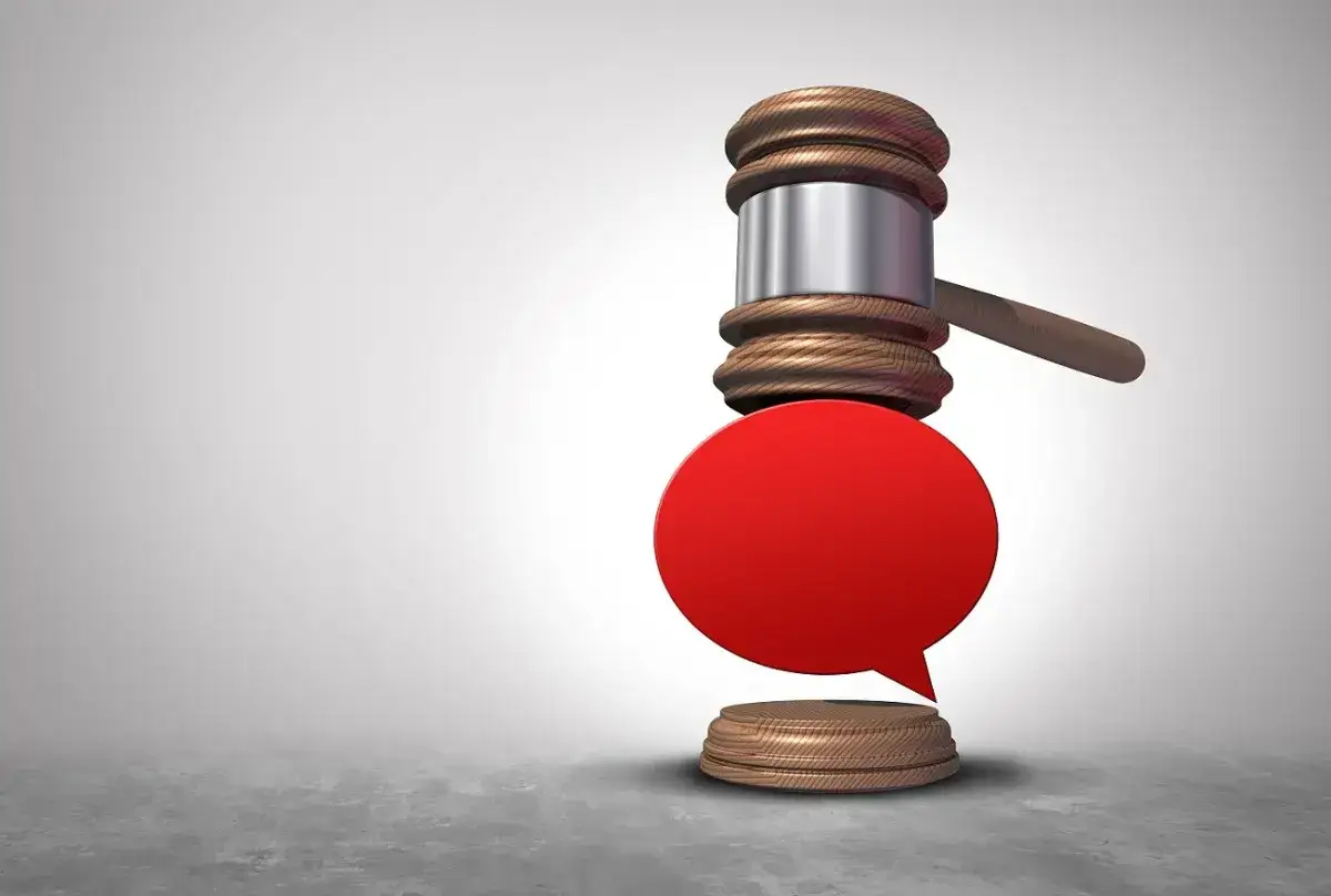 Młotek sędziowski nad pustym dymkiem symbolizuje, że słowa mogą prowadzić do pomówienia i zniesławienia.