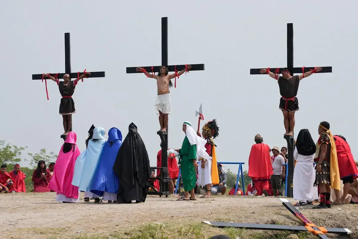 Filipińczycy odgrywają scenę ukrzyżowania. Trzech mężczyzn na krzyżach, otoczonych przez ludzi w kolorowych i czarnych szatach.